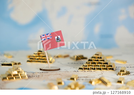 Miniature Bermuda flag on a world map with numerous gleaming gold bars, representing global finance, offshore investment, wealth management, and international business opportunities 127168910