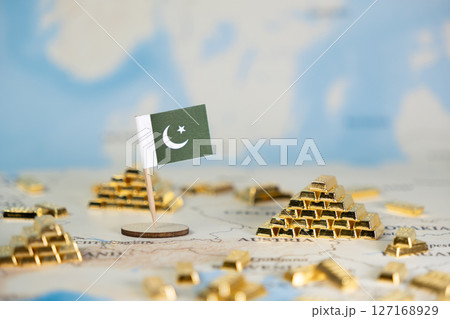 Miniature Pakistan flag and gold bars on a world map symbolize national wealth, economic growth, and global finance, offering ample copy space 127168929