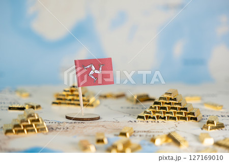 Isle of Man flag and stacked gold bars on a blurred map symbolize offshore finance, global wealth, and international economic strategy with copy space 127169010