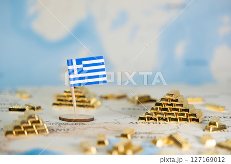 Greek flag standing on a map with many gold bars, symbolizing national wealth, economic stability, and financial reserves, with ample copy space 127169012