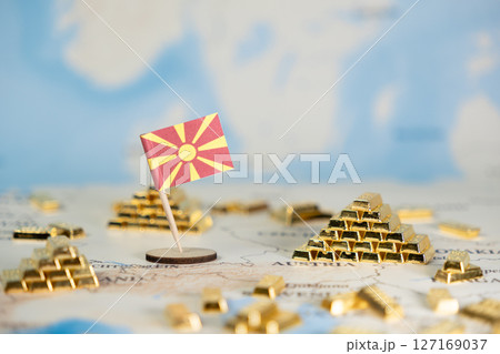 North Macedonia flag stands on a map with gold bar stacks, symbolizing national wealth, economic power, and global market influence, offering clear copy space 127169037