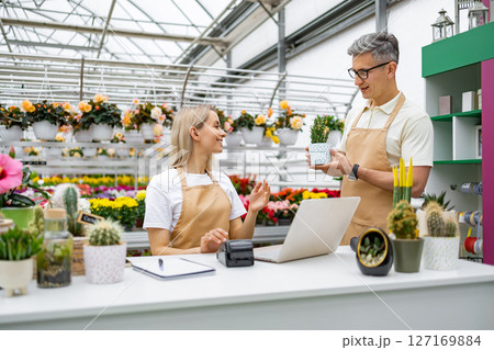 A Caucasian man and woman are in a flower shop, interacting with each other while looking at a small plant. 127169884