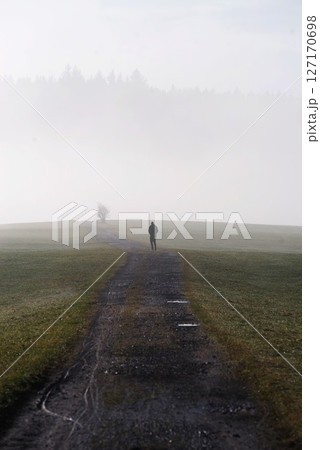 Man is walking down a path in a foggy field Man is walking down a path in a foggy field 127170698