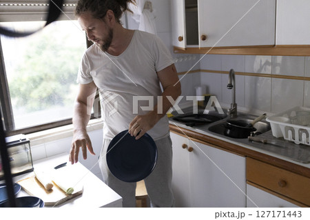 Man preparing ingredients and picking up plate in kitchen 127171443