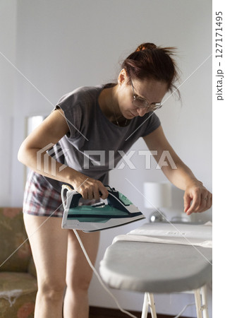 Woman ironing clothes on ironing board at home 127171495