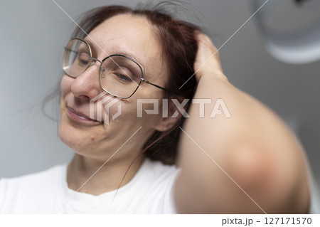 Woman wearing glasses touching her hair and smiling gently 127171570