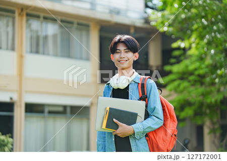 A cheerful Asian college student stands outside on campus with a backpack, smiling and looking at the camera. A cheerful Asian college student stands outside on campus with a backpack, smiling and looking at the camera. 127172001