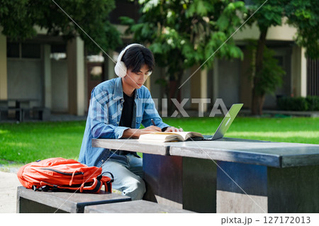 Portrait of a young Asian male college student e-learning using laptop on the bench on campus. Portrait of a young Asian male college student e-learning using laptop on the bench on campus. 127172013