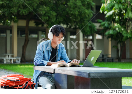 Portrait of a young Asian male college student e-learning using laptop on the bench on campus. Portrait of a young Asian male college student e-learning using laptop on the bench on campus. 127172021