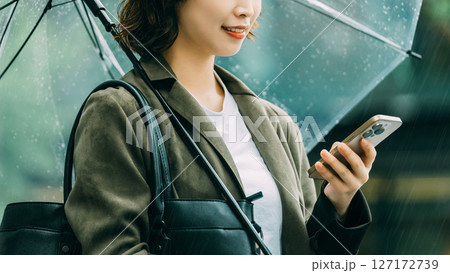 傘をさしてスマホを使う女性（梅雨・6月） 127172739