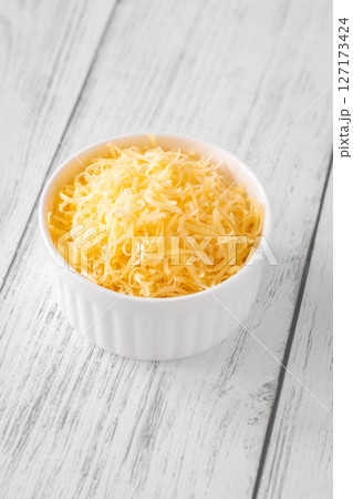 Finely grated cheddar cheese fills white bowl with vibrant golden orange shreds 127173424