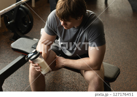 Close up shot of man at gym holding protein shaker. Bodybuilder during strength training. Fitness healthy lifestyle concept. Hydration after workout session. Supplement product Close up shot of man at gym holding protein shaker. Bodybuilder during strength training. Fitness healthy lifestyle concept. Hydration after workout session. Supplement product 127176451