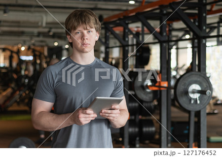 Serious personal trainer or bodybuilder standing wearing gray t-shirt holding tablet or clipboard in gym or fitness center. Coach making exercise plan in gym Serious personal trainer or bodybuilder standing wearing gray t-shirt holding tablet or clipboard in gym or fitness center. Coach making exercise plan in gym 127176452