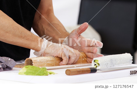 Chef Preparing Sushi Roll Using Bamboo Mat on a Clean Work Surface 127176547