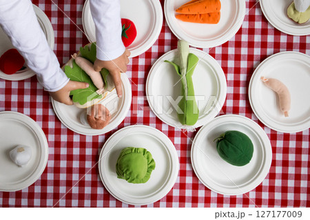 Child hands arranging fabric vegetables on picnic table with red white checkered tablecloth 127177009