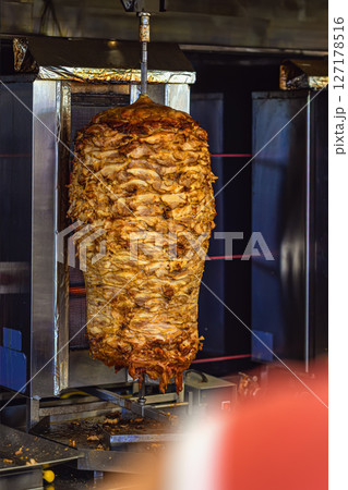 Vertical stack of roasted meat on rotating spit in shawarma grill machine. Concept of street food, traditional cuisine and fast food preparation with authentic taste 127178516