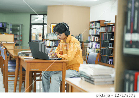 Attractive young male university student using a laptop while studying in library. Attractive young male university student using a laptop while studying in library. 127178575