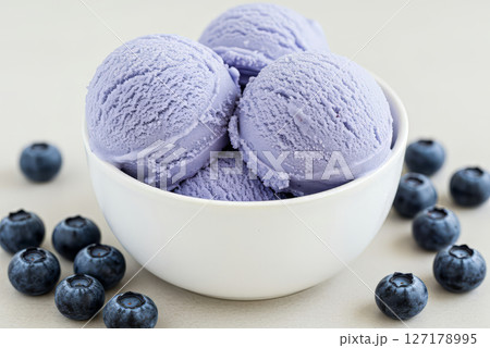 Close-up of a white bowl filled with three scoops of blueberry ice cream, garnished with a blueberry berries.  127178995