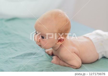 One-month-old baby lying on tummy and curiously observing surroundings. Infant tummy time for neck strength, cognitive development, and early exploration. Parenting and newborn growth concept One-month-old baby lying on tummy and curiously observing surroundings. Infant tummy time for neck strength, cognitive development, and early exploration. Parenting and newborn growth concept 127179876