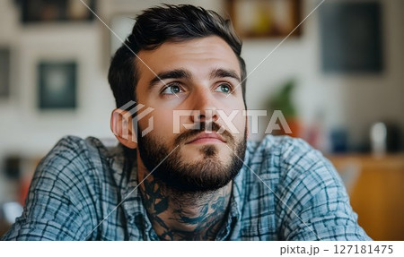 Pensive man with neck tattoo gazes upwards in soft, diffused lig 127181475