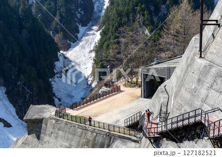 快晴の春、雪山と森林に囲まれた黒部ダムの外階段を観光客が降りていく風景 快晴の春、雪山と森林に囲まれた黒部ダムの外階段を観光客が降りていく風景 127182521