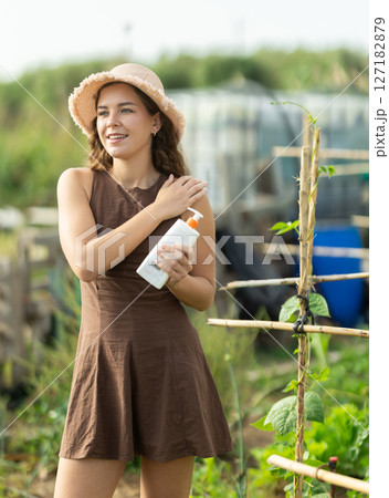 Young woman applying sunscreen in cottage garden 127182879