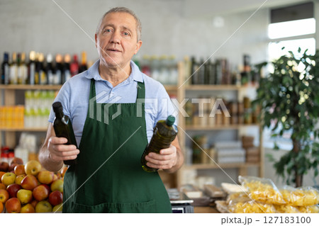 Elderly man seller offers olive oil in grocery store Elderly man seller offers olive oil in grocery store 127183100