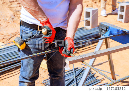 Construction worker grips metal rebar cuts while wearing gloves on busy building site. 127183212