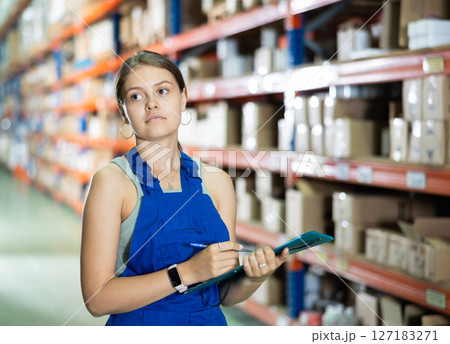 Attentive female manager keeps records of construction materials in warehouse, writing down data on paper 127183271