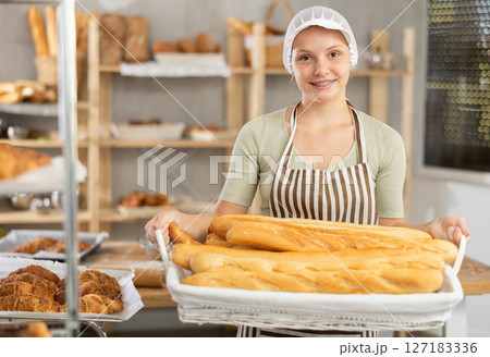 Portrait of female baker holding a basket of baguettes and fresh bread in hands 127183336