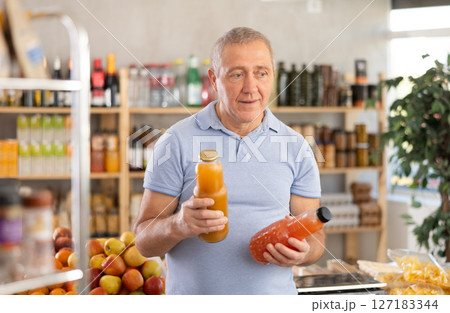 Mature man hold white plastic bottles and choose consider juice in store Mature man hold white plastic bottles and choose consider juice in store 127183344