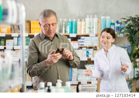 Man with phone chooses medicines with help of pharmacist Man with phone chooses medicines with help of pharmacist 127183414