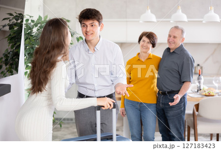 Cheerful young guy greeting wife returning home from trip Cheerful young guy greeting wife returning home from trip 127183423