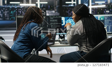 Data center coworkers doing brainstorming, using artificial intelligence machine learning models to configure equipment. IT experts cooperating in server farm, working on optimizing systems, camera B Data center coworkers doing brainstorming, using artificial intelligence machine learning models to configure equipment. IT experts cooperating in server farm, working on optimizing systems, camera B 127183471