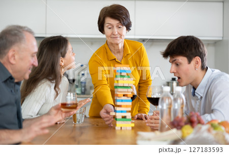 Smiling adult woman or Mother having fun enjoying tower building game with husband and adult children at comfortable family home Smiling adult woman or Mother having fun enjoying tower building game with husband and adult children at comfortable family home 127183593