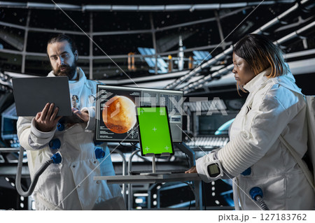 Orbital station coworkers analyzing Mars planetary data using green screen tablet. Team of astronauts in spaceship doing red planet surface research using chroma key device 127183762