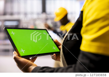 Manufacturing engineer presenting a tablet with isolated copyspace in industrial workspace. Selective focus of device displaying blank chromakey screen held by smart factory employee. Manufacturing engineer presenting a tablet with isolated copyspace in industrial workspace. Selective focus of device displaying blank chromakey screen held by smart factory employee. 127183838