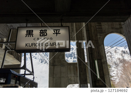 黒部平駅の看板とコンクリートの建物、雪に覆われた立山連峰とロープウェイが見える晴天の景色 黒部平駅の看板とコンクリートの建物、雪に覆われた立山連峰とロープウェイが見える晴天の景色 127184692