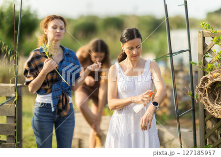 Three women applying repellent in cottage garden 127185957