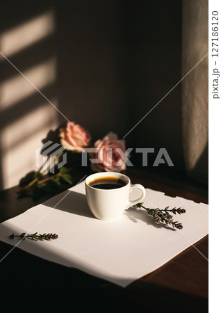 White coffee cup on blank paper, bathed in sunlight and shadows. Pink roses and lavender add beauty. Ideal for cozy, aesthetic, and peaceful morning. 127186120