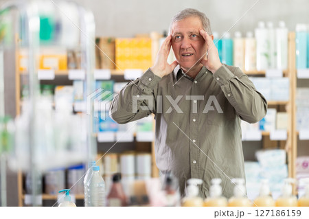Senior man with headache looking for medicine in pharmacy 127186159