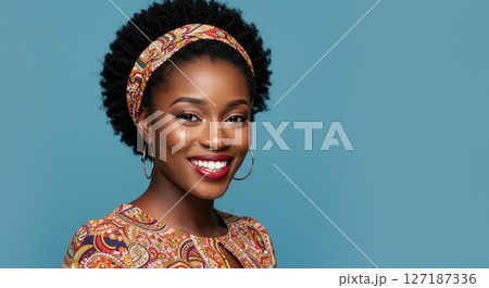 Confident African Woman Smiling in Colorful Outfit with Headband Against Blue Background 127187336