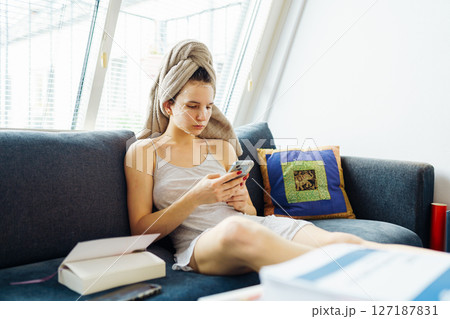 woman with towel on head using smartphone sitting on comfortable sofa woman with towel on head using smartphone sitting on comfortable sofa 127187831