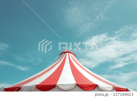 Red and white circus tent roof with flags against blue sky 127189023