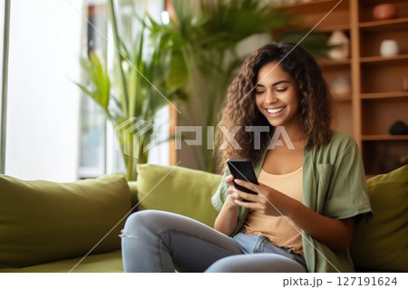 Joyful Young Latin Woman Engaging with Her Phone on a Home Sofa. Generative ai 127191624