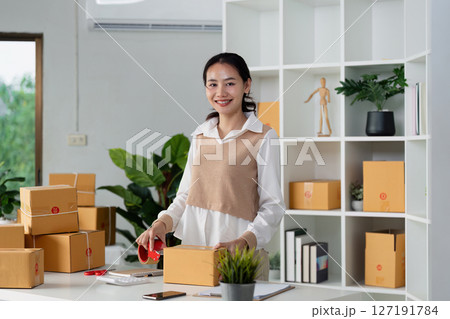 Young business entrepreneur sealing a box with tape. Preparing for shipping, Packing, online selling, e-commerce concept 127191784