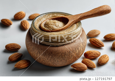 Creamy almond butter in rustic wooden jar with wooden spoon, surrounded by whole almonds on light background 127191797