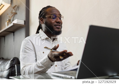 Young African American business man working with laptop and document on desk and talking on mobile at home Young African American business man working with laptop and document on desk and talking on mobile at home 127192029