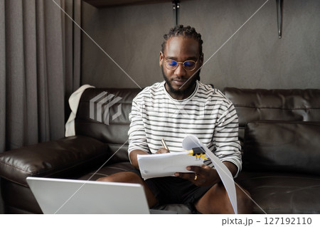 African American business man working with document and laptop at home on couch. work from home concept 127192110