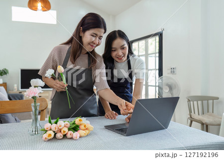 mother and daughter arrange flowers together as a hobby. mother and daughter spend free time doing flower arranging activities together and looking at laptop 127192196